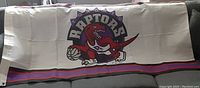 Photo showing the full Toronto Raptors flag laid flat, highlighting the dinosaur logo and team colors.