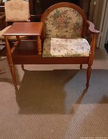 Full front view of vintage wooden gossip bench chair showing floral fabric upholstery and attached wooden writing surface.