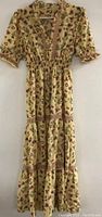 Beige floral patterned long dress with short puffed sleeves and V-neck hanging on a wall.