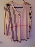 Light beige women's long sleeve v-neck top with multi-color plaid pattern hanging on hanger.