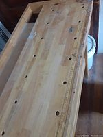 Close-up of work bench surface showing multiple round holes and ruler marks for measuring and securing items.