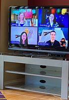Sony Bravia TV powered on displaying a multi-window video call screen, sitting on a TV stand with storage compartments and cable management cutouts.