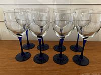 Eight blue stemmed wine glasses arranged in two rows on a wooden surface.
