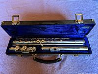 Full open view of the Armstrong Model 104 flute disassembled into three parts placed inside the original hard shell case lined with blue velvet.