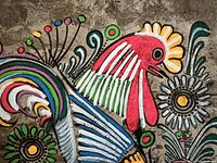 Close-up of colorful Mexican bark painting featuring a red rooster with abstract floral elements on bark surface.
