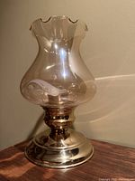 Side view of vintage brass hurricane lamp showing polished brass base and clear fluted glass chimney with scalloped edge and etched pattern.