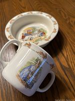 Close-up of a double handled mug with rabbits in various poses and a rabbit pushing a pram illustration on the side.