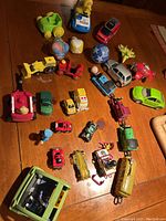 Overall view of assorted children's toys arranged on wooden surface showing cars, planes, trucks and figures.