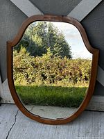 Full view of curved vintage wood mirror reflecting outdoor greenery and concrete floor.