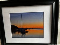 Framed photograph showing sunset scene with sailboats on calm water, signed by Jill Fitz Hirschbold.
