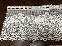 Close-up image of lace curtain panel with houses and trees pattern
