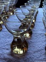 Close-up side angle of iridescent glassware showing the distinctive amber-colored sturdy bases of the glasses with delicate wide rims.