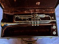 Overhead view of trumpet in open brown velvet-lined hard shell case including trumpet and two mouthpieces