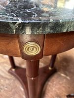 Close-up of decorative brass-colored medallion accent on wooden frame below marble top of side table.