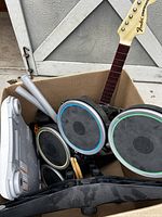 Top view of box containing Rock Band guitar controller neck and drum set pads with drumsticks and pedal