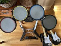 Top view of drum kit drum pads arranged in a circle on stand, includes pedal and 2 wooden drumsticks on floor beneath.