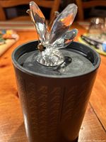 Close view of Swarovski crystal butterfly placed on the black round packaging lid, showing butterfly's clear faceted wings and body