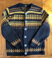 Front view of the brown and mustard yellow Norwegian knit sweater laid flat on a wooden surface showing overall pattern and button closure.