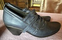 Side view of black leather wedge shoes with strap and overlap design in lightly used condition.