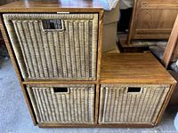 Wooden storage unit featuring three beige woven wicker slide-out baskets arranged in two rows, with the right basket on the bottom row slightly lower due to staggered layout.