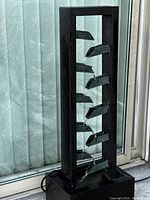 Front view of the black metal waterfall indoor fountain with water flowing down the angled trays inside a rectangular frame.