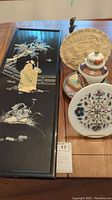 Overview of Asian themed decorative items including lacquer panel, carved plate, ginger jar, and floral inlay plate