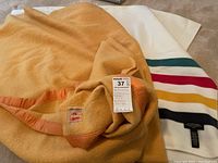 Photo showing both blankets, one white with colored stripes and the other solid mustard color.