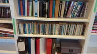 Books and binders on three shelves including a mix of colors and sizes, showing titles and book types.