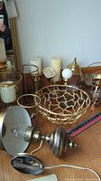 Photo of several brass decorative items including electric wall light fixture, candle holders, decorative bowl, and candles on wooden floor.