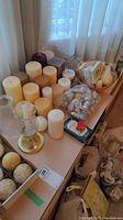 Various pillar candles of different sizes and colors placed on a windowsill along with batteries, a glue tool, and other art supplies visible nearby.