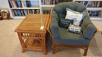 Overall view of cane table and armchair with cushions and pillows before bookshelf