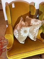 Front view of mustard yellow wingback chair with two floral cushions on seat.