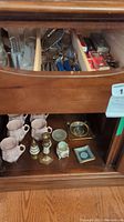 Cabinet shelf with fine china mugs, candle holders, and small decorative trays.