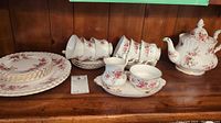 Set of cups, saucers, plates, creamer, and teacups shown on wooden shelf with floral rose design and gold accents