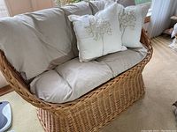 Front view of the wicker loveseat with beige cushions and three embroidered floral decorative pillows.