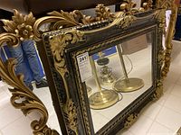 Large rectangular resin frame mirror with intricate gold and black detailing on the frame, featuring floral and swirl designs.