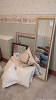 Photo of three mirrors including a large gold framed full-length mirror, a medium brown framed mirror, and a smaller textured framed mirror with assorted decorative pillows stacked in front of them