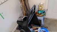Wheelbarrow with various garden tools leaning against wall, showing gloves, soil bag, and miscellaneous garden accessories.