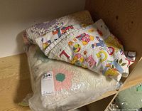 Photo showing folded quilts including one with pastel floral hexagonal patches and one with alphabet cartoon prints