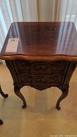Full view of wood side table showing curved legs, carved drawers, and top surface.