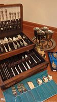 Wooden flatware chest open displaying ornate silver plated forks, knives and spoons on two tiers