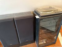 Pair of black Technics speakers and black cabinet with audio components inside and a Hitachi turntable on top