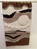 Full view of woven yarn wall hanging with abstract design in brown, beige, cream, and black yarns.