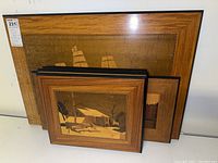 Photo of four wood art wall hangings stacked showing a large sailing ship piece in the back and three smaller cabin scenes in front