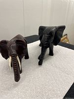 Two wood carved elephant figurines on white cloth, showing front view and tusks