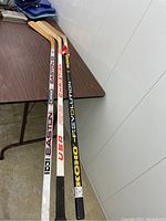 Three hockey sticks standing side-by-side showing painted shafts with Easton, Christian Koho, and Koho Revolution branding.