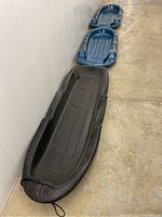View of three winter sleds, two blue smaller sleds stacked and one large black sled beside them.