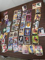 Assorted sports trading cards laid out on a wooden surface featuring hockey, basketball, baseball, football, and soccer cards.