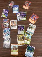 Top view of 18 assorted Bakugan trading cards laid out on a wooden surface, showing various colorful characters and stats.