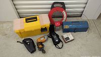 Yellow and blue toolboxes with multitester, BBQ igniter kit, drill, and other hand tools arranged on floor